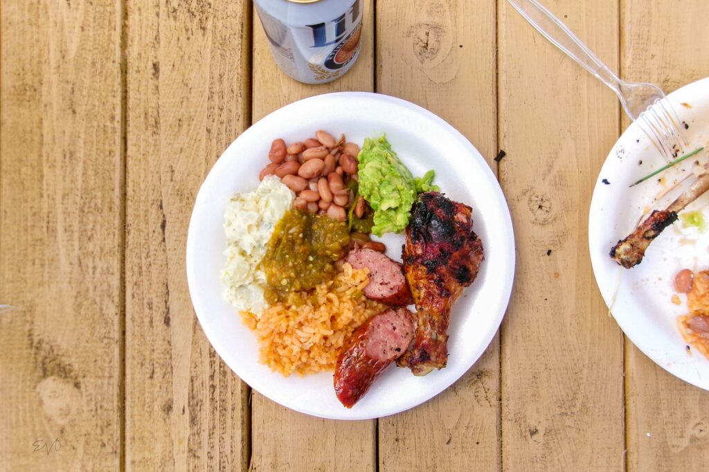 Appetizing BBQ meal with chicken, beans, guacamole, rice, and sausage on a wooden table.