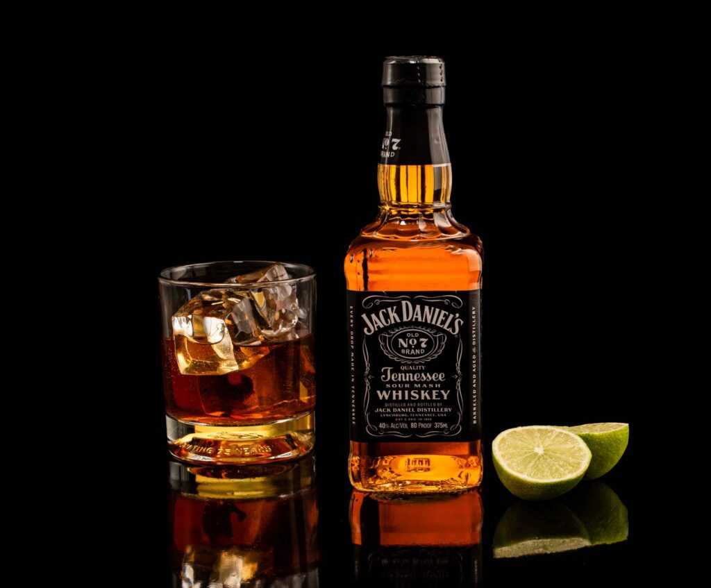 Classic Jack Daniel's whiskey with glass and lime on reflective black surface.