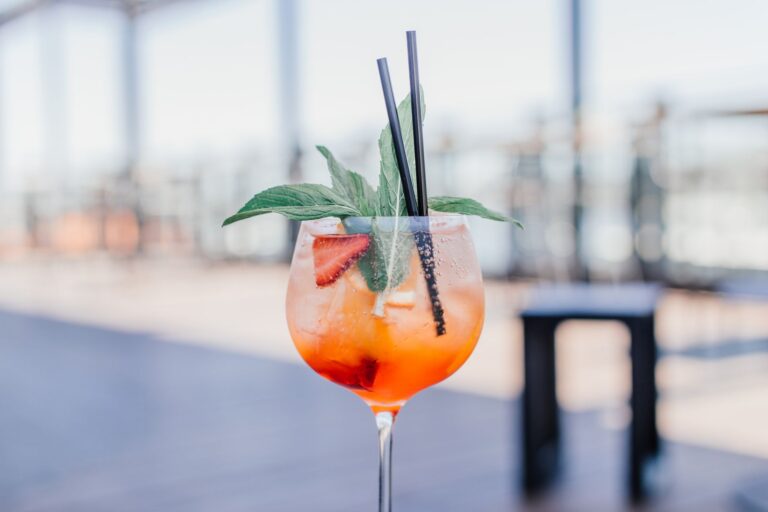 Close-up of a vibrant orange cocktail garnished with mint and strawberry, served in a glass with straws.